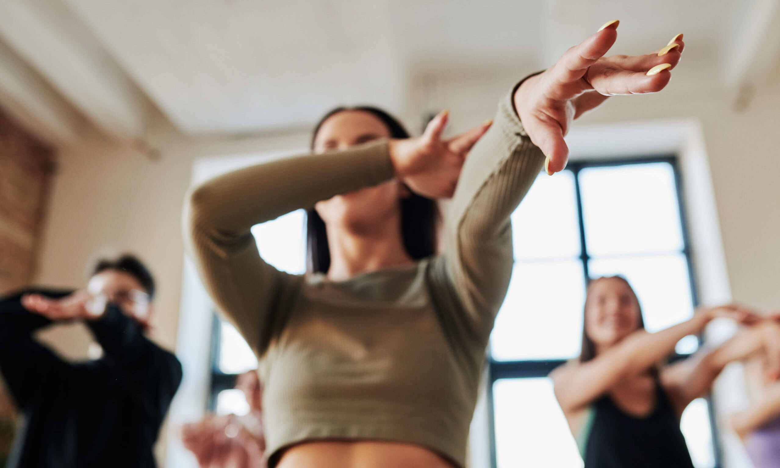 Hands of dynamic teenage girl stretching arms during vogue dance movement while showing it to group of youthful performers