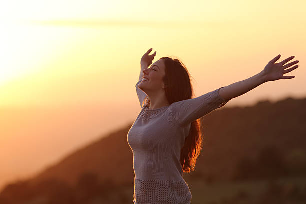 Backlit of a woman at sunset breathing fresh air raising arms